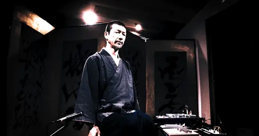書が並ぶ空間で尺八を構える演奏者